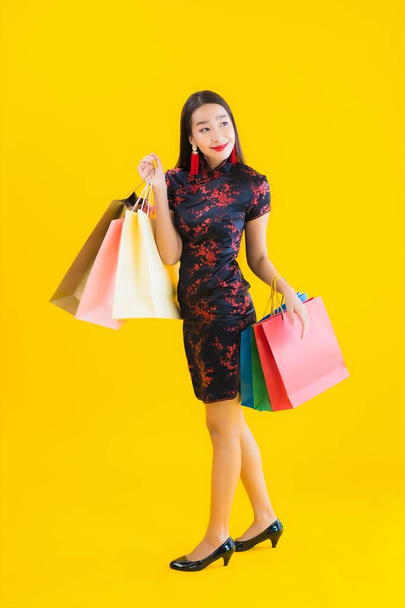 Portrét krásná mladá asijská žena nosit čínské šaty s nákupní taškou, chytrý mobilní telefon, kreditní karta pro čínské Nový rok na žlutém izolovaném pozadí - Fotografie, Obrázek