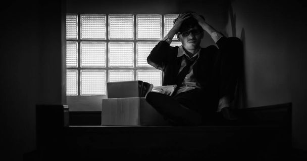 Кавказский работник, сидящий на лестнице делового офиса компании с отчаянным чувством безработицы во время кризиса коронавирусного ковида 19 блокировка в черно-белом - Фото, изображение