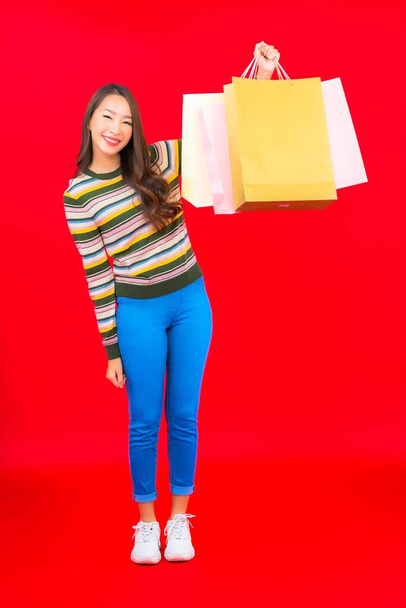 Renkli alışveriş çantası ve kırmızı arka planda kredi kartıyla güzel bir Asyalı kadın portresi - Fotoğraf, Görsel