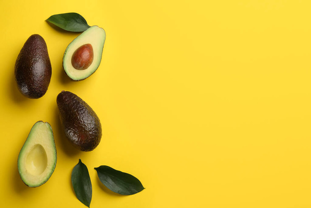 Whole and cut ripe avocadoes with green leaves on yellow background, flat lay. Space for text - Fotó, kép