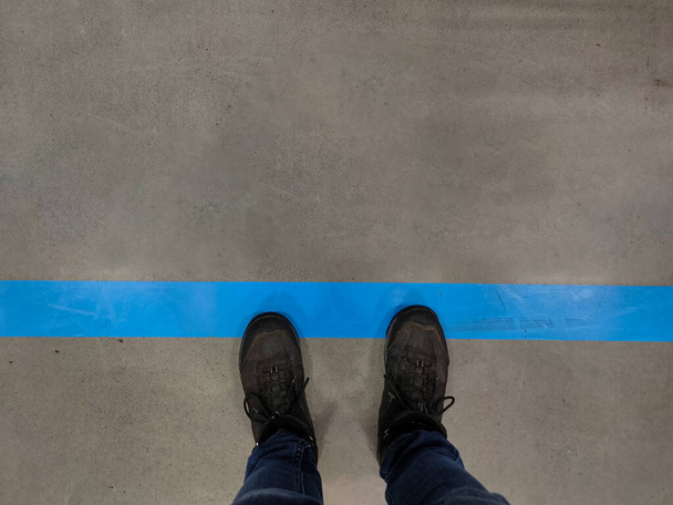 Обувь стоит рядом с синей линией в магазине, чтобы держать социальное дистанцирование в очереди - Фото, изображение