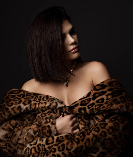 Portrait of young rich sexy brunette woman in leopard fur coat with deep neckline over naked body with expensive jewelry - Photo, Image