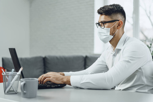 Young businessman sitting at his working desk with medical mask on - Φωτογραφία, εικόνα