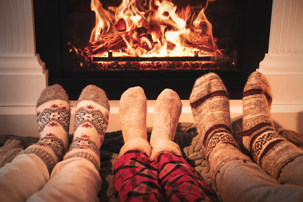 Lovely family in warm socks resting near fireplace at home, closeup - Foto, afbeelding