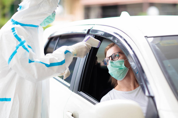 Koronaviruksen nenäpyyhkäisynäyte. Hazmat-pukuinen lääkäri ottaa sylkinäytteen covid-19 diagnostiikkaan autossa. Nainen kuljettaja potilas drive-thru testausasemalla sairaalassa. Virusepidemia. - Valokuva, kuva