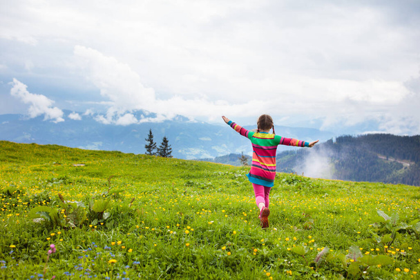 Children hiking in Alps mountains. Kids look at snow covered mountain in Austria. Spring family vacation. Little girl on hike trail in blooming alpine meadow. Outdoor fun and healthy activity. - Photo, Image