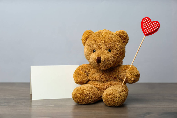 Cute teddy bear with red heart and blank card on wooden table. Valentine's day celebration - Фото, зображення