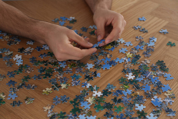 Man playing with puzzles at wooden table, closeup - Photo, Image