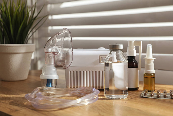 Nebulizador moderno com máscara facial e medicamentos em mesa de madeira dentro de casa. Equipamento para inalação - Foto, Imagem