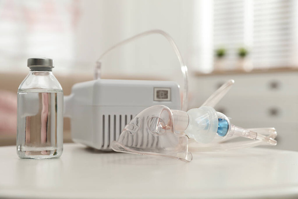Modern nebulizer with face mask and liquid medicine on white table indoors. Inhalation equipment - Фото, зображення