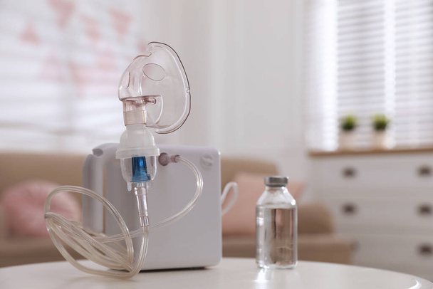 Modern nebulizer with face mask and liquid medicine on white table indoors. Inhalation equipment - Fotó, kép