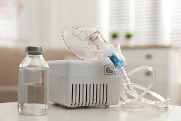 Modern nebulizer with face mask and liquid medicine on white table indoors. Inhalation equipment - Photo, Image