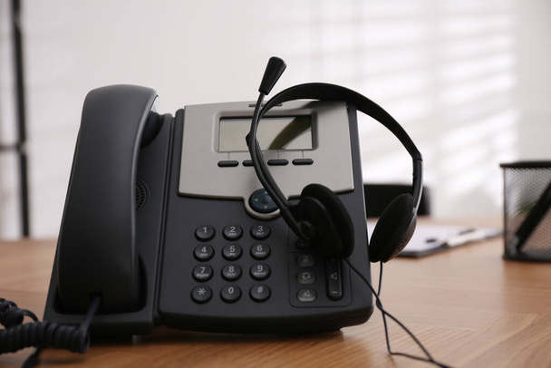 Desktop telephone and headset on wooden table in office. Hotline service - Fotó, kép