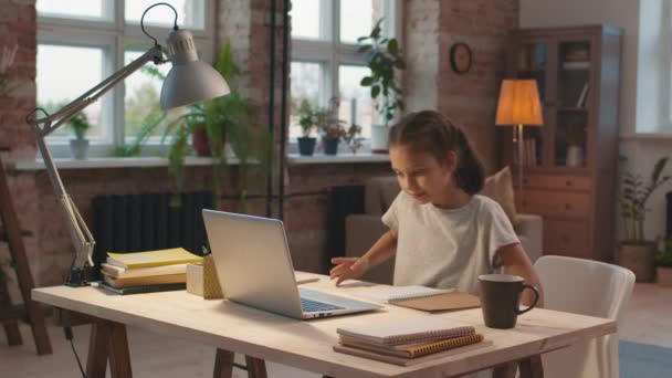 Plan moyen avec ralentissement de la petite fille assise au bureau dans le salon et étudiant en ligne - Séquence, vidéo