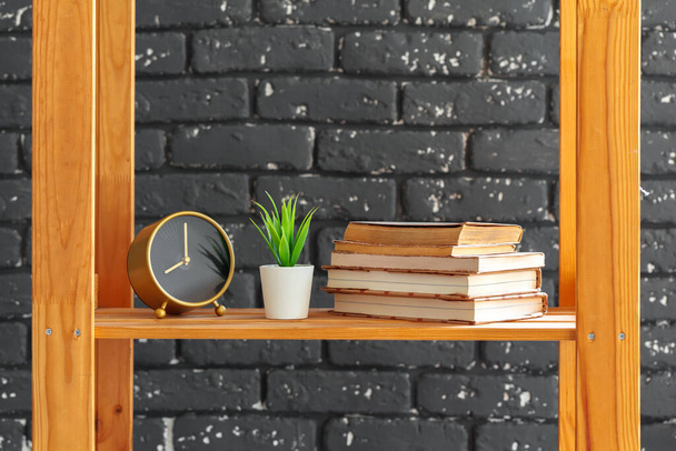 Wooden bookshelf with books and stuff against black brick wall - Foto, imagen
