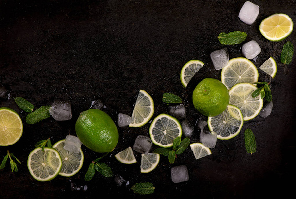 Hortelã fresca, limão e gelo sobre um fundo preto. Ingrediente para mahito. Vista superior - Foto, Imagem