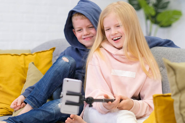 Kids bloggers talking with followers, live streaming, looking to smartphone screen at home. Boy and Girl making selfie or call friends and parents. Social media, instagram, stay home and quarantine - Fotó, kép