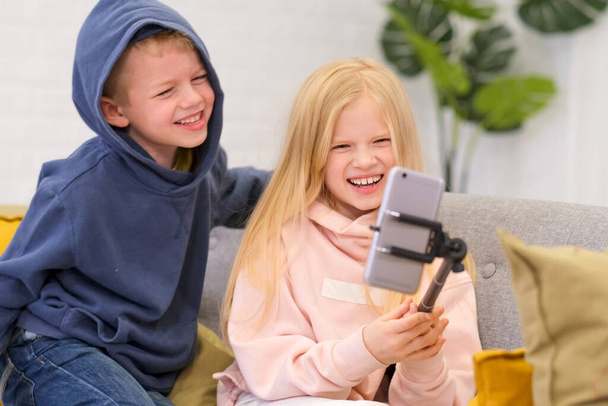 Kids bloggers talking with followers, live streaming, looking to smartphone screen at home. Boy and Girl making selfie or call friends and parents. Social media, instagram, stay home and quarantine - Foto, immagini