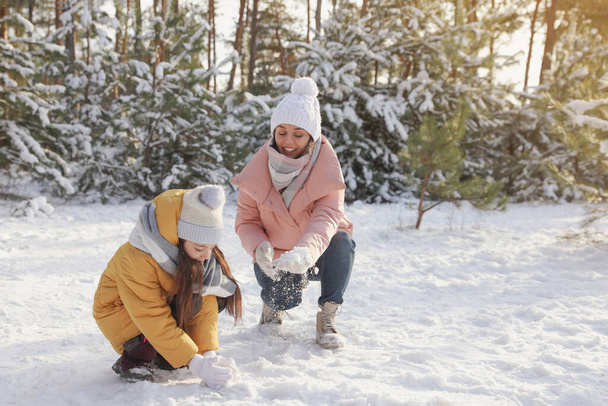 Mother and daughter rolling snowballs in winter forest - Foto, Bild