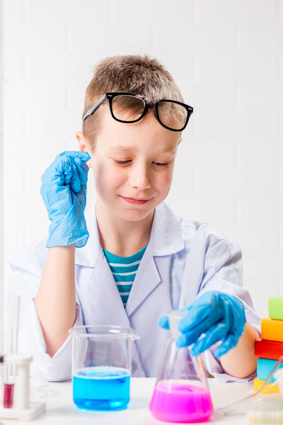 Koulupoika tutkii monivärisiä aineita koeputkissa, tekee kokeita muotokuva valkoisella taustalla. Konsepti koronaviruksen tutkimiseksi laboratoriossa - Valokuva, kuva