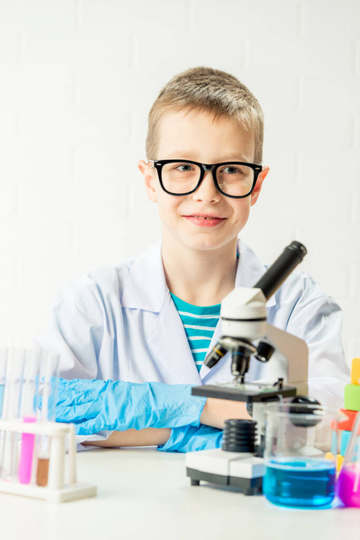 顕微鏡を持った少年は試験管の中で化学物質を検査し、白い背景の肖像画である実験を行います。研究室でのコロナウイルスの研究のための概念 - 写真・画像