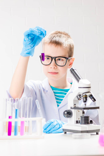 A schoolboy with a microscope examines chemicals in test tubes, conducts experiments - a portrait on a white background. Concept for the study of coronavirus in the laboratory - Foto, Imagen