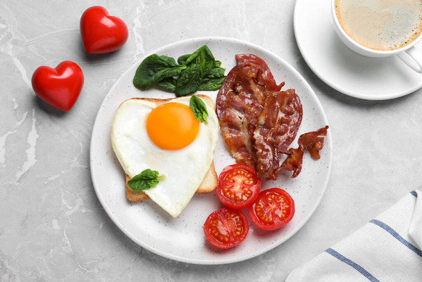 Romantic breakfast with fried bacon and heart shaped egg on grey table, flat lay. Valentine's day celebration - Fotó, kép