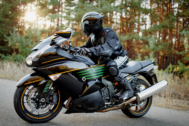 Motocyklista jedzie leśną drogą. Baw się dobrze na pustej drodze na sportowym motocyklu. Kopiuj miejsce na spersonalizowany tekst - Zdjęcie, obraz