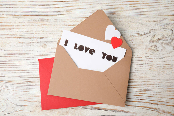 Card with phrase I Love You in envelope and paper hearts on white wooden table, flat lay - Foto, immagini