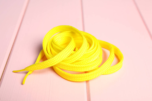 Yellow shoelace on pink wooden background. Stylish accessory - Fotó, kép