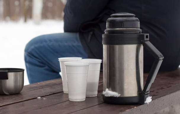 thermos avec des tasses sur un banc en hiver après une partie de thé dans la nature. - Photo, image
