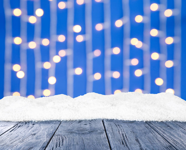 Wooden surface with heap of snow and blurred Christmas lights on background, bokeh effect  - Foto, Imagen