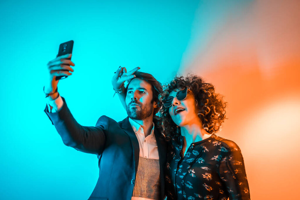 Party lifestyle, a Caucasian couple taking a selfie at a party with orange and blue lights - Foto, Imagen