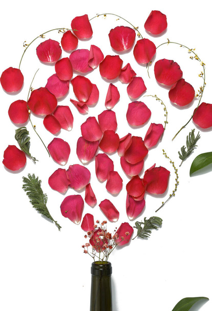 Rosenblätter und Zierpflanzen platzen aus dem Flaschenhals. Frauentag, blumige Weinaromen. Kopierraum. isoliert auf weiß. flache Lage. - Foto, Bild