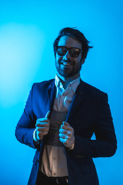 Studio lifestyle, a handsome young Caucasian man in a session with elegant clothes and sunglasses, with neon blue light - Fotó, kép