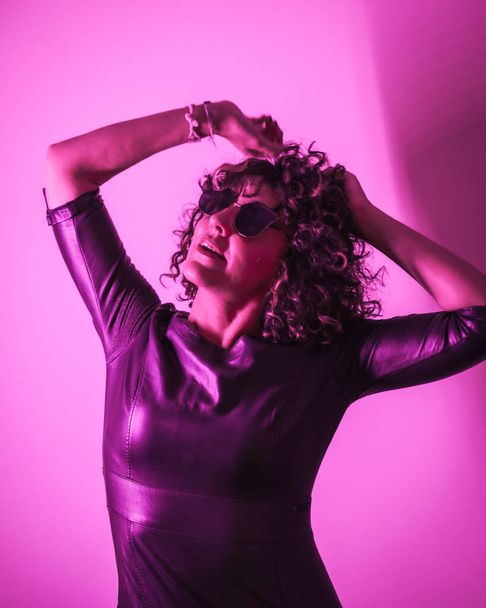 Studio lifestyle, a young Caucasian woman having a lot of fun in a photo session with elegant clothes and sunglasses, with neon pink light - Foto, Imagem