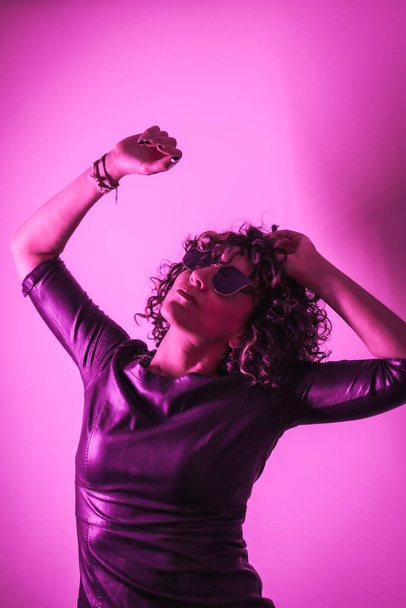 Studio lifestyle, a young Caucasian woman looking up in a photoshoot with elegant clothes and sunglasses, with neon pink light - Foto, afbeelding