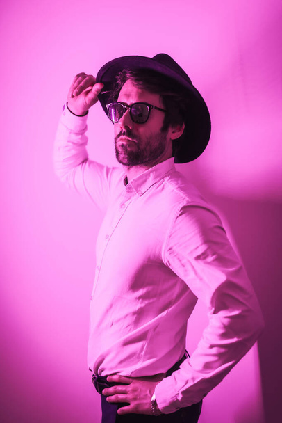 Studio lifestyle, a young Caucasian man with a seductive look in a photo session with sunglasses, with neon pink light - Фото, изображение