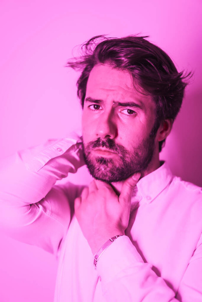 Studio lifestyle, portrait of a Caucasian man with seductive gaze in a white shirt, illuminated with a pink neon light - Fotografie, Obrázek