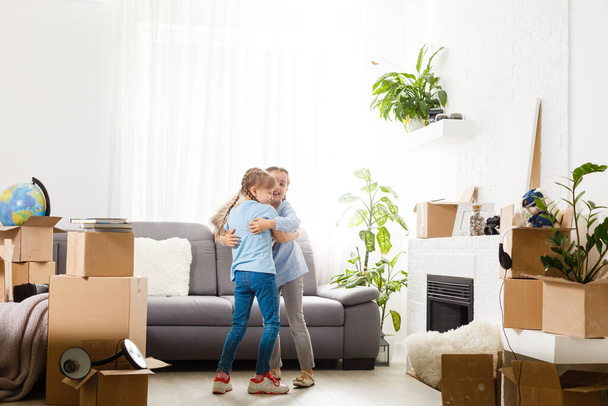 Две маленькие дочери празднуют день переезда, взволнованы переездом в новый дом, смеются гостиную с картонными коробками - Фото, изображение