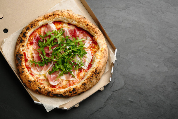 Tasty pizza with meat and arugula in cardboard box on black table, top view. Space for text - Foto, afbeelding