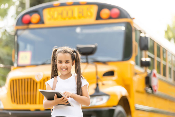Tyttö, jolla on reppu keltaisen koulubussin lähellä. Liikenne opiskelijoille - Valokuva, kuva