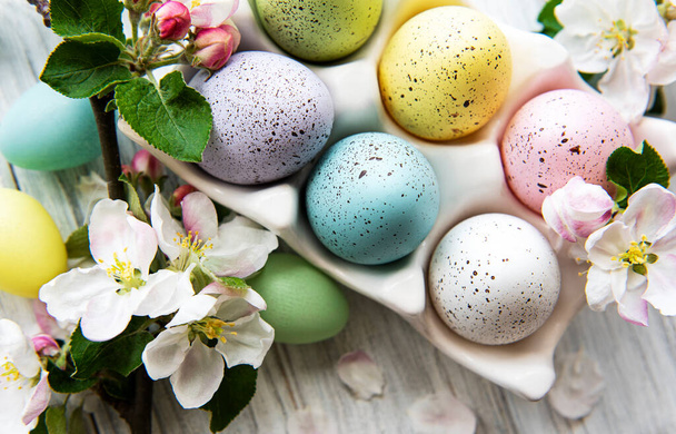 Κάτοψη των βαμμένων πασχαλινών αυγών και του δίσκου αυγών σε λευκή ξύλινη επιφάνεια - Φωτογραφία, εικόνα