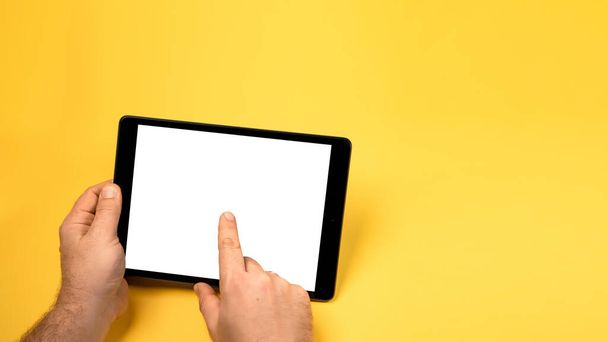 Gesneden close-up view mock up afbeelding man hand houden zwarte tablet pc wit blanco scherm geïsoleerde gele heldere achtergrond. Digitaal modern gadget, afstandsbediening concept. Vrije lege ruimte voor tekst - Foto, afbeelding