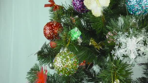 Uma árvore de Natal decorada com um gerland e brinquedos está girando em um fundo leve - Filmagem, Vídeo