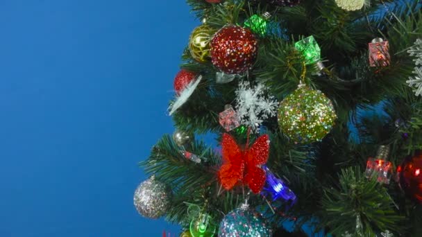 Árvore de Natal decorada com um gerland piscando e pêras multi-coloridas em um fundo azul - Filmagem, Vídeo