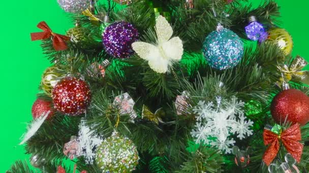 Karácsonyfa díszített villogó koszorúk és gyönyörű játékok forog a zöld háttér - Felvétel, videó