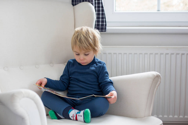 Mother and child, toddler boy, reading a book, sitting in a cozy armchair in bedroom - Photo, image