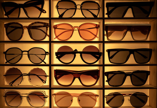 σιλουέτες γυαλιών ηλίου διαφόρων σχημάτων σε πάγκο σε κατάστημα στο σκοτάδι - Φωτογραφία, εικόνα