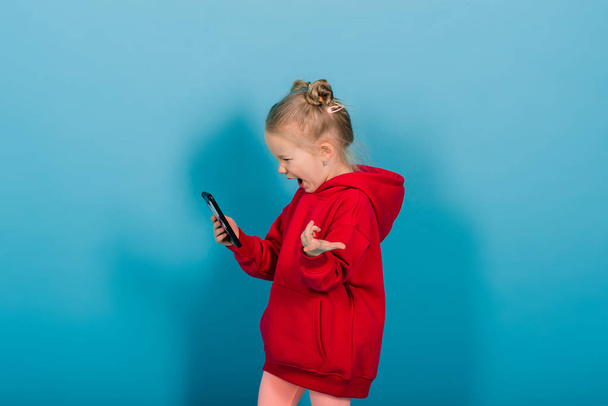 Hymyilevä pieni tyttö puhelimessa sinisellä taustalla - Valokuva, kuva